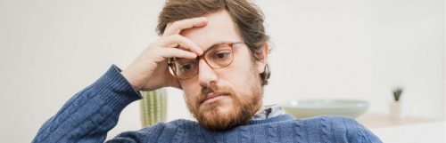 man hand on forehead wistful eyes sits in living room worrying thinking about his emotions