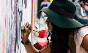 long curly black hair woman with green hat joins gravity paints on street wall