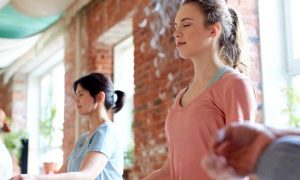 group of woman eyes closes sits leg crossed concentrates on meditation in quiet room