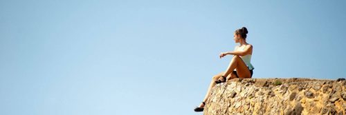woman sits on rock looking blue clear sky