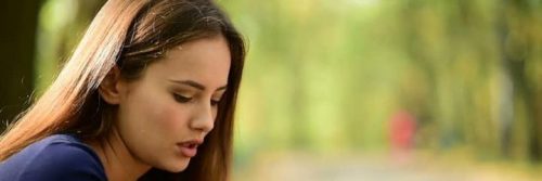 woman sits in park looking downward