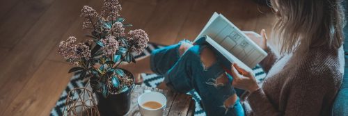 woman sits on floor beside side table tea cup reading book