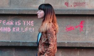 woman walks on street beside wall having pink gravity detailing fear is the mind killer