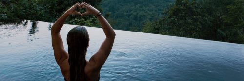 woman stands in swimming pool two hands making heart shape