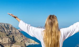 woman gratitude earth blue ocean sky white shirt blonde coast rocks