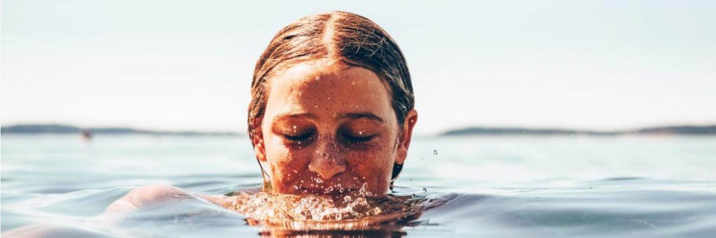 young woman eyes closed swimming ocean water in cloudy sky