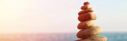 balanced stone rocks facing blue ocean in sunny sky