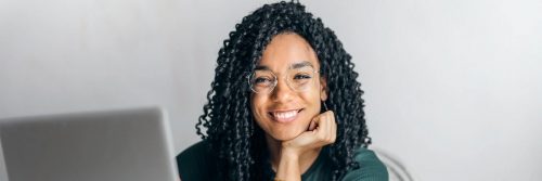 woman hand on chin sitting beside laptop smiling