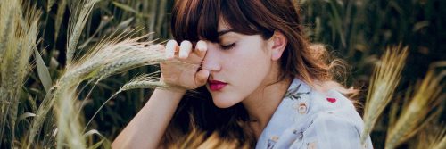 woman sits beside trees closing eyes thinking feeling overwhelmed