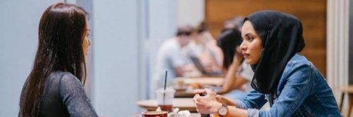 two women sits in office talking to each other