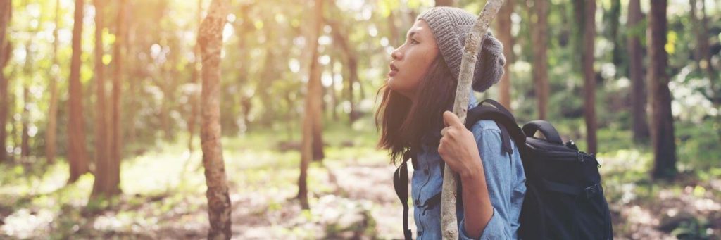 young woman holds tree stick hiking in forest