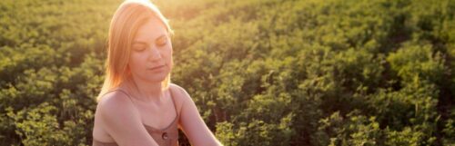 woman looks downward sits on green field in beautiful sunny sky