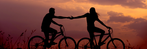 couple shadow rides two bikes hand in hand in beautiful sunset