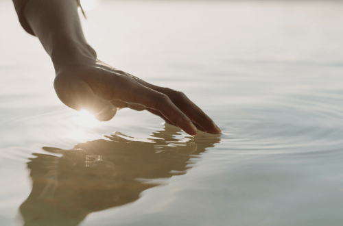 persons hand touching the ocean in beautiful light for the Wave of Abundance