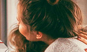 two women hug beside white giftbox wrapped by red banner
