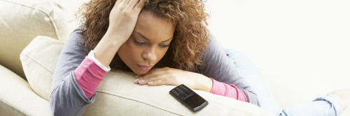 woman sadly sits on white couch looking at old model cellphone worrying