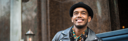 happy man with black fedora dark blue jacket stands alone smiling