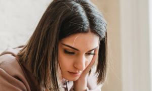woman with sad face hands on face looks downward