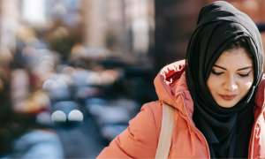 woman wears black hoodie and light pink raincoat face down walks alone