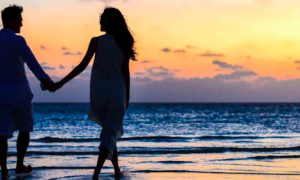 couple hand in hand happily walks along beach in sunset sky